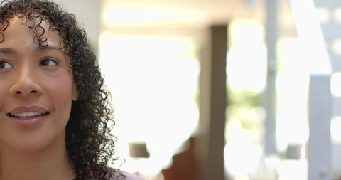 Backlit headshot of young woman smiling and looking up with curly hair and nose stud