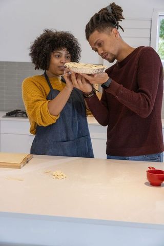 African american couple checking raw lattice pie at kitchen island while baking together