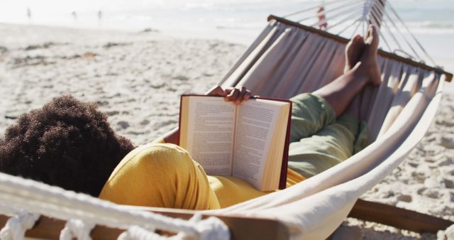 Person reclining on a hammock enjoying a book by the seaside, perfect for depicting vacation, relaxation, and leisure scenes. Ideal for travel advertisements, beach resorts, and lifestyle blogs.