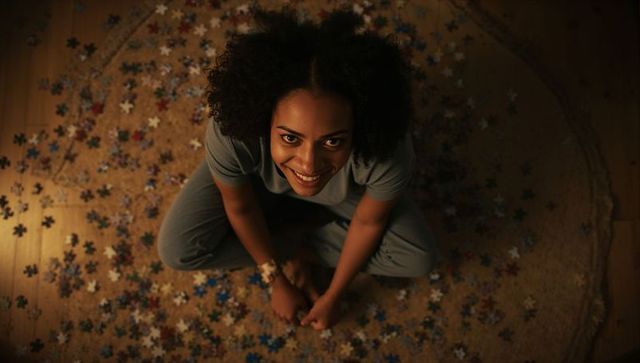 Smiling woman sitting on woven rug assembling jigsaw puzzle in cozy evening light