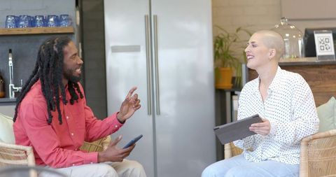 Diverse coworkers chatting in modern kitchenette sharing tablet and smartphone