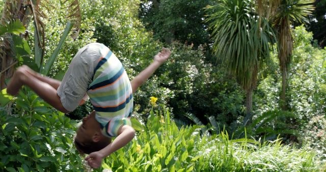 Young boy enjoying a summer day, performing a somersault in a green, lush garden. Ideal for themes of childhood joy, outdoor activities, summer fun, and acrobatics.