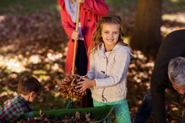 Young girl collecting autumn leaves with family in park. Ideal for themes of family bonding, outdoor activities, seasonal changes, and childhood fun. Perfect for use in advertisements, blogs, and articles about family activities, nature, and fall season.