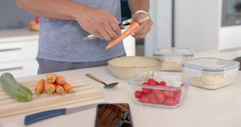 African man peeling carrot while meal-prepping in bright modern kitchen interior