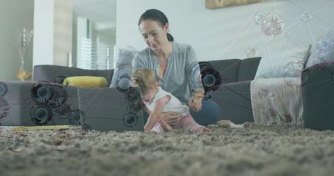 Mother bonding with infant on living room carpet using laptop with tech network overlay