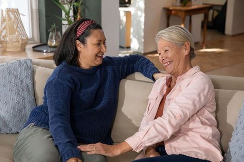 Warm companionship between diverse senior women sharing conversation on cozy sunlit sofa