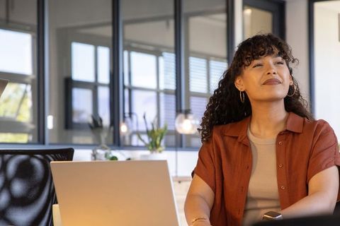 Confident woman working at laptop in modern open-plan office with glass partitions