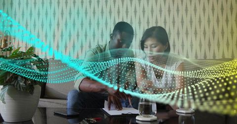 Couple collaborating on couch with notebook and smartphone amid glowing digital data wave