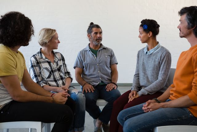 This image shows a group of diverse friends engaged in a discussion during an art class. They are seated in a circle, fostering a sense of community and collaboration. This image can be used for educational materials, teamwork and collaboration concepts, community building, and creative workshops.