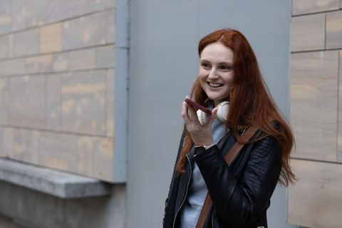Redhead woman talking on smartphone smiling with headphones and leather jacket on city sidewalk