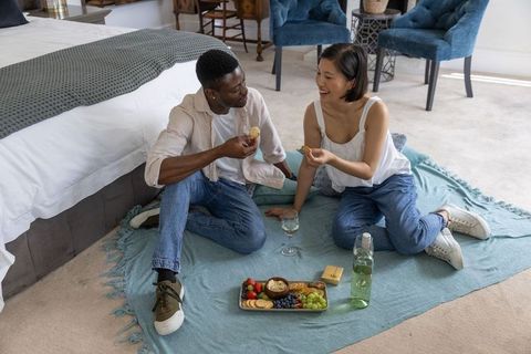 Couple enjoying cozy indoor picnic on bedroom blanket sharing wine and charcuterie