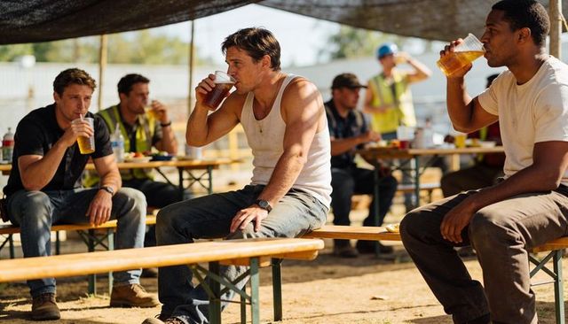 Construction workers taking break under shade tent drinking amber beverages on benches