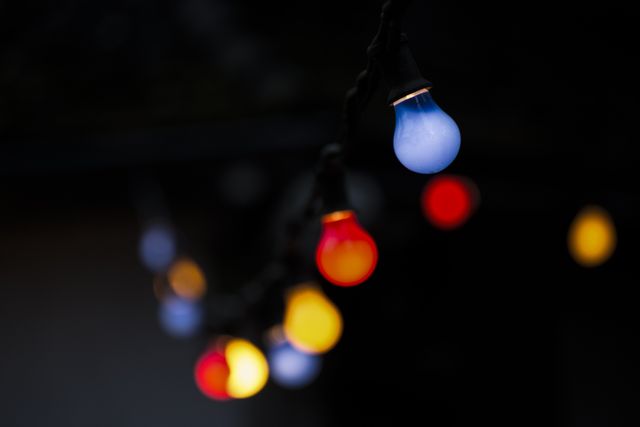 String lights feature red, blue, and yellow glowing bulbs contrasted against a dark background. Ideal for themes of celebration, nightlife, festive decor, atmospheric lighting, holiday decorations, backyard parties, wedding decor, and cozy ambiance. Suitable for promotional banners, event invitations, holiday season advertisements, and interior design blogs.