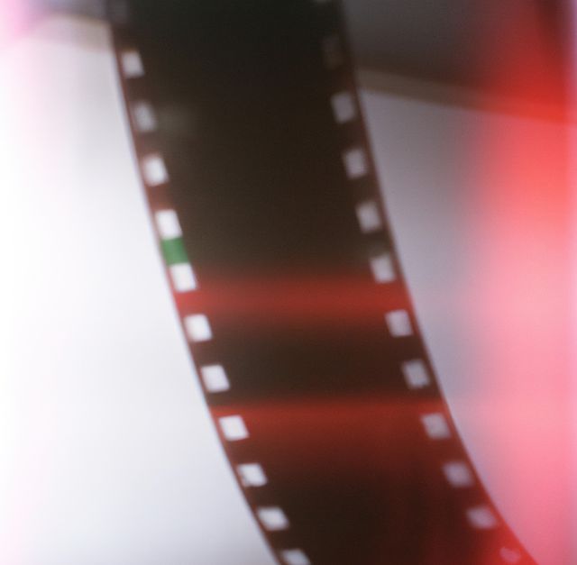 Showing a close-up of a damaged film strip with noticeable light leaks and a red tint. The abstract appearance and nostalgic feel make it suitable for use in projects emphasizing vintage photography, creativity, and film culture. It can be featured in website designs, poster art, or as a background element in multimedia presentations focusing on analog photography.