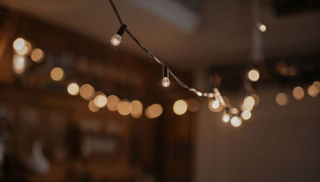 Cozy amber string lights hanging diagonally with glowing bokeh and warm wood backdrop