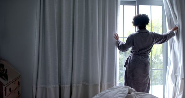 Back of biracial woman in bathrobe opening curtains in bedroom, copy space - Download Free Stock Photos Pikwizard.com