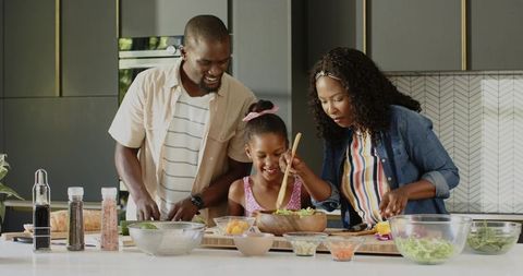 African American family preparing healthy salad together at modern kitchen island