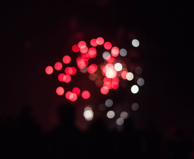 Bright red and white fireworks blurred to form colorful bokeh patterns in the night sky. Ideal for festive and celebratory themes, this scene conveys fun and excitement. Perfect for use in holiday, festive event promotions, or city tourism advertisements.
