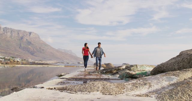 Happy diverse couple walking on pier and holding hands with copy space by sea. Outdoors, summer, vacations, relaxing, free time, love and togetherness, unaltered.