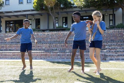 Children playing barefoot on school lawn holding hands during outdoor recess