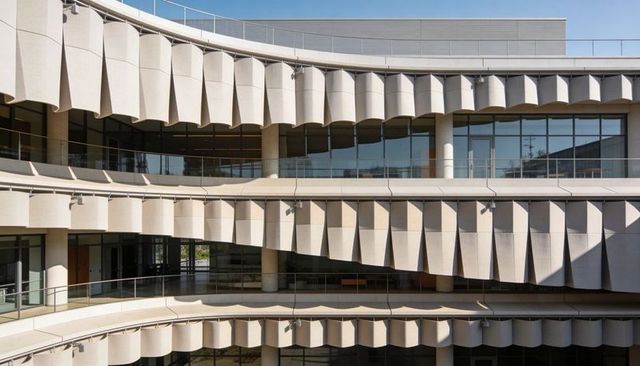 Curved multi-level facade casting diagonal shadows with concrete fins and glass rails