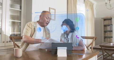 Senior couple reviewing finances and planning at home with futuristic holographic tablet ui