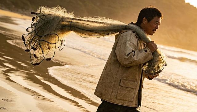 Fisherman walking golden hour beach carrying fishing net with floats on wet shoreline