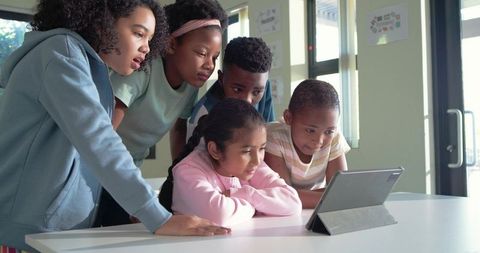 Diverse students gathering around tablet for collaborative learning in bright classroom