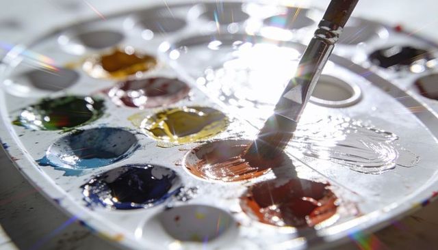 Backlit wet watercolor palette with round-tipped brush mixing vibrant glossy pigments