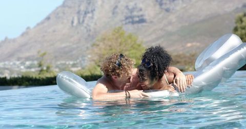Couple enjoying romantic embrace on silver float in infinity pool with mountain view