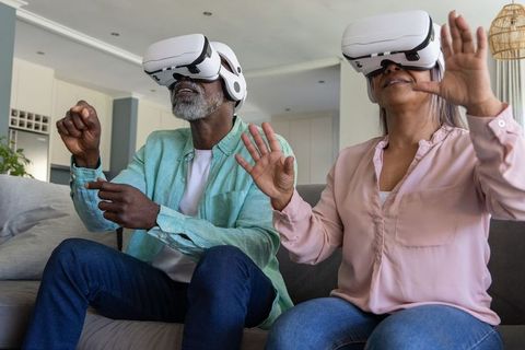 Mature African American Couple Using Virtual Reality Headsets on Sofa in Modern Home