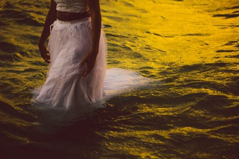 Mystical women in white dress walking in golden water