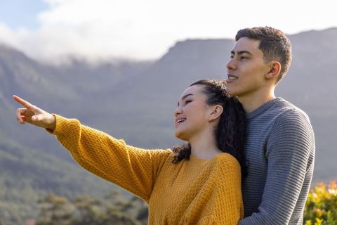 Young couple embracing and pointing on scenic mountain ridge overlooking misty valley