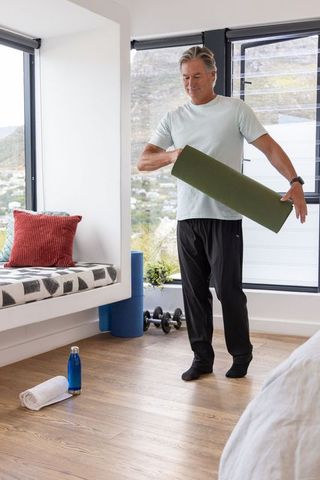 Mature man preparing yoga mat in bright home workout nook for daily stretching and fitness