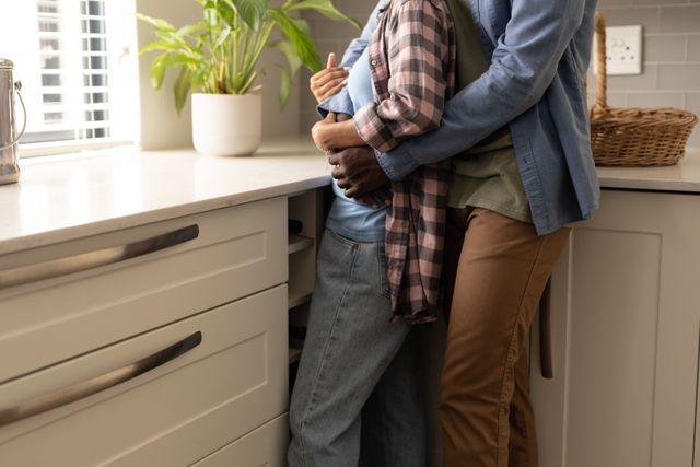 Midsection of african american young man embracing girlfriend while standing by kitchen counter. romance, unaltered, lifestyle, home, love and togetherness concept.