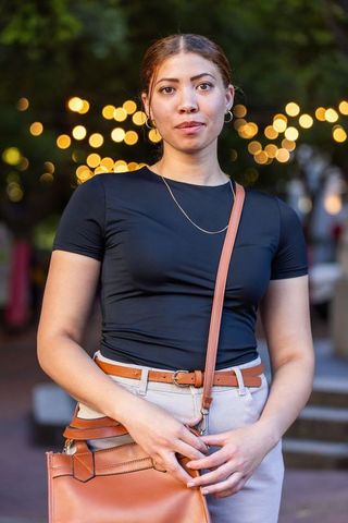 African american woman standing at dusk with bokeh lights, black top and tan crossbody