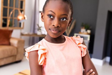Thoughtful young girl standing arms crossed, gazing sideways in modern living room
