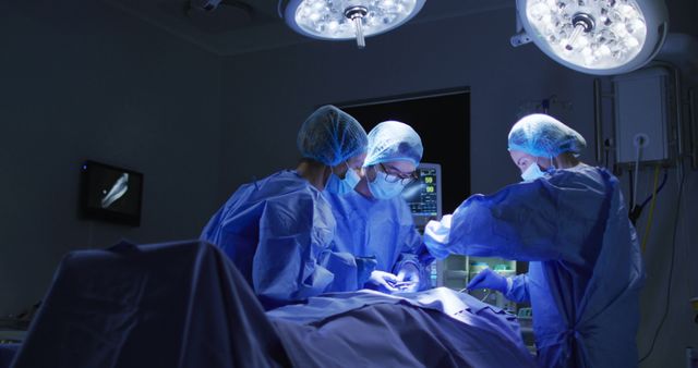 Surgeons are intensely performing an operation in a sterile and well-lit operating room. They are dressed in standard surgical attire, including masks, gowns, and gloves. Bright surgical lights overhead highlight the precision and care required in medical operations. This is useful for medical-related articles, surgical procedure descriptions, health care imagery, and educational material on surgery.