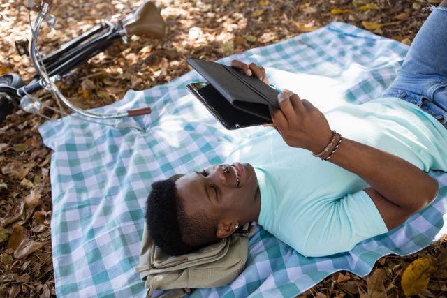 Man using digital while lying on a picnic blanket in the park