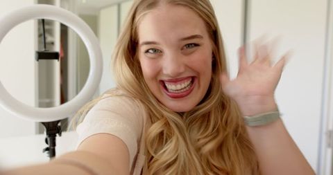 Joyful influencer woman waving during livestream in home studio