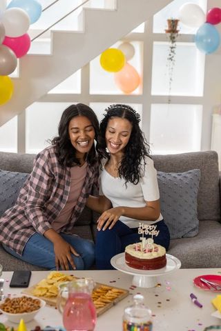 Two friends celebrating 18th birthday with red velvet cake and pastel balloons at home