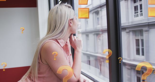 This image depicts a blonde woman in an office environment, looking out of a window while deep in thought. It can be used to represent themes of reflection, contemplation, career decisions and business aspirations. Suitable for articles or advertisements dealing with professional development, business growth, introspection, motivational content, or corporate environments.