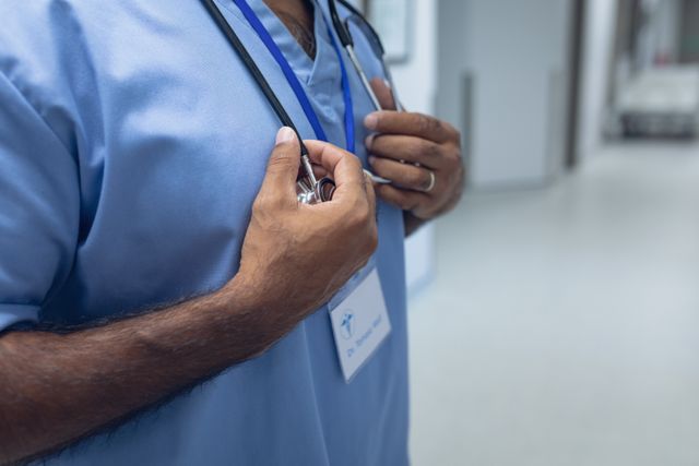 Mid section of biracial male doctor standing with stethoscope in the corridor at hospital