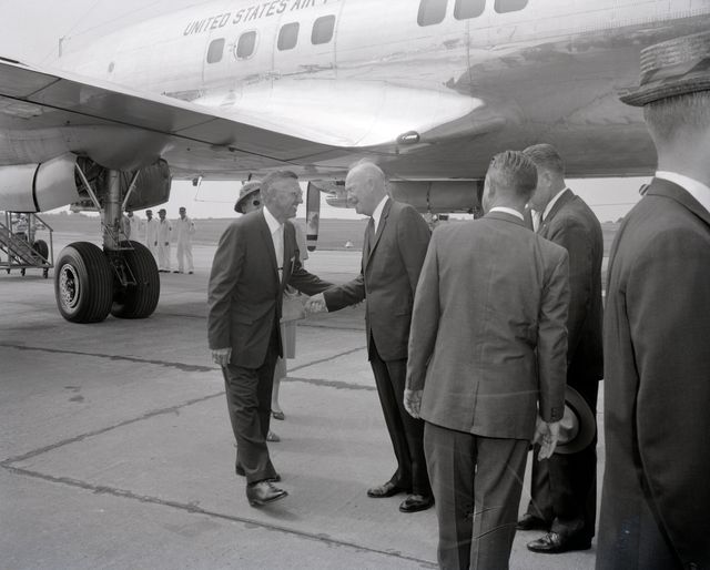 President Dwight D. Eisenhower, standing near a United States Air Force plane, shakes hands with an official during his visit to the Marshall Space Flight Center for its dedication. The photograph captures a moment of diplomacy and history in the 1960s. This image could be ideal for articles or presentations about significant historical events, presidential visits, or the early years of the space age.