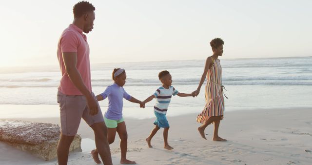 Family of four enjoying a peaceful walk on the beach at sunset. Ideal for advertisements or promotions related to travel, family bonding, vacations, or beach activities.