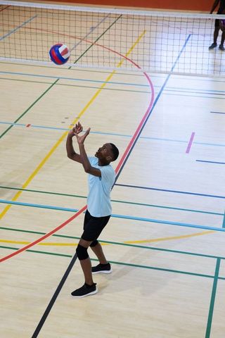 Teenage african american volleyball player preparing to set ball near net in indoor gym practice