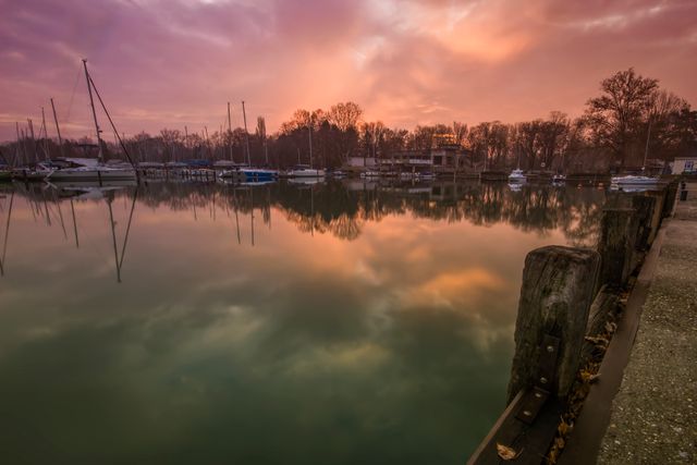 Sunrise scene with colorful sky reflecting on calm water at a quiet harbor with boats docked. Serene early morning atmosphere perfect for relaxation, nature, and waterfront themes. Ideal for backgrounds, travel brochures, calendars, peaceful and soothing visuals.