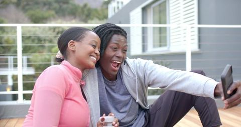 African American Couple Taking Selfie on Balcony Laughing in Casual Athleisure Outfit