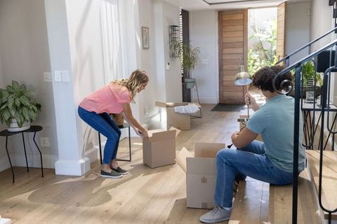 Young couple unpacking boxes in modern entryway carrying lamp and arranging furniture