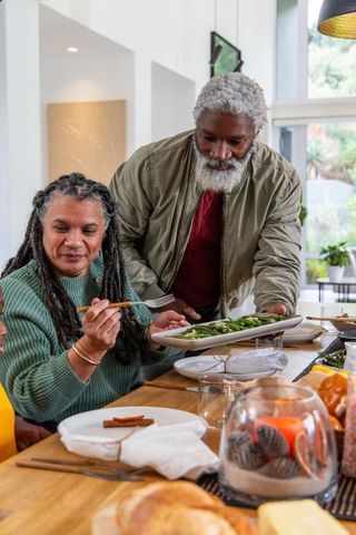 African american senior couple sharing healthy meal passing platter of greens modern dining table